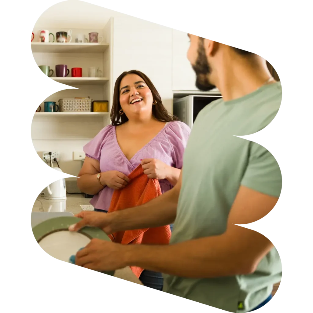 Two people smiling at each other while doing dishes in kitchen