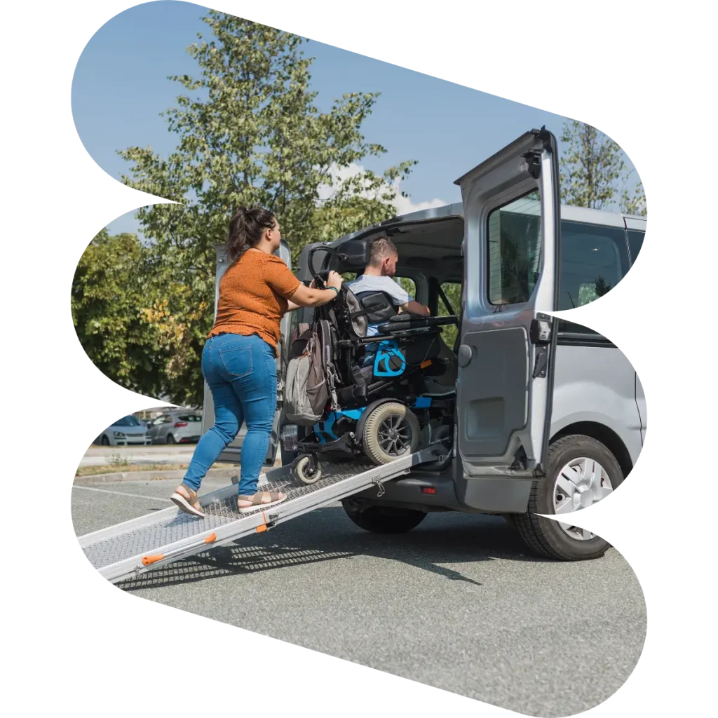 Support worker pushing man in wheelchair into disability van