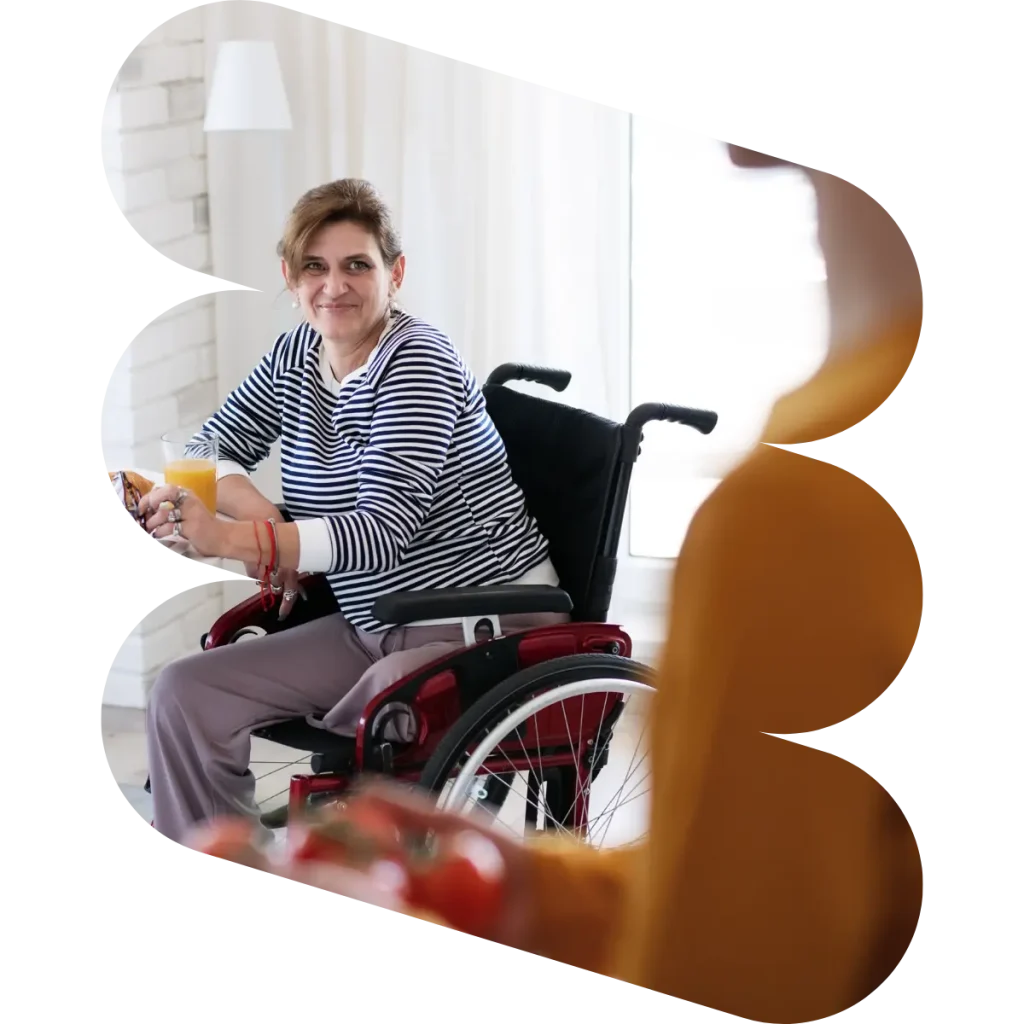 Disabled woman in wheelchair sitting in kitchen at home, smiling and looking at support worker